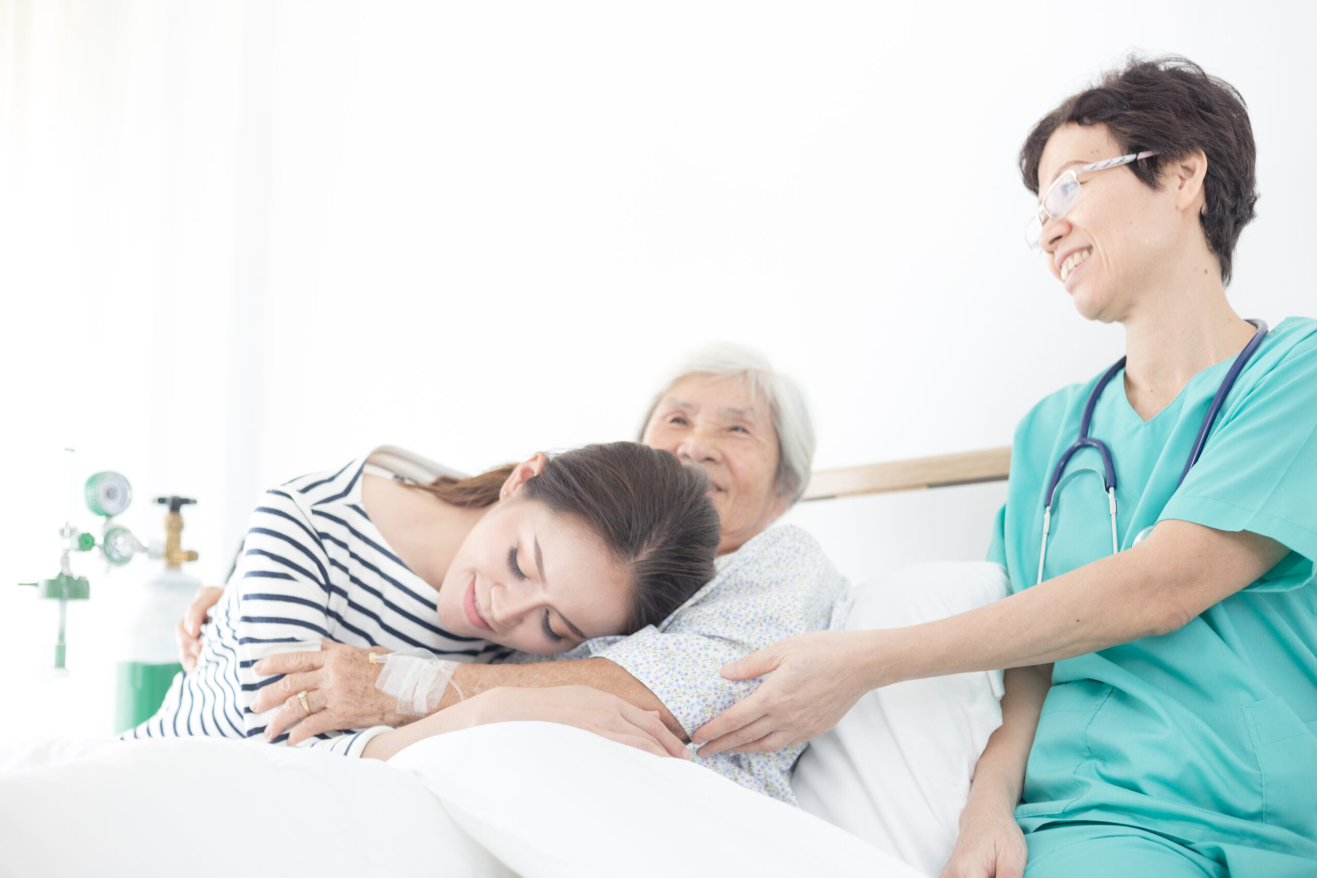 Paciente anciana sonriendo en la cama siendo consolada por su hija y una doctora