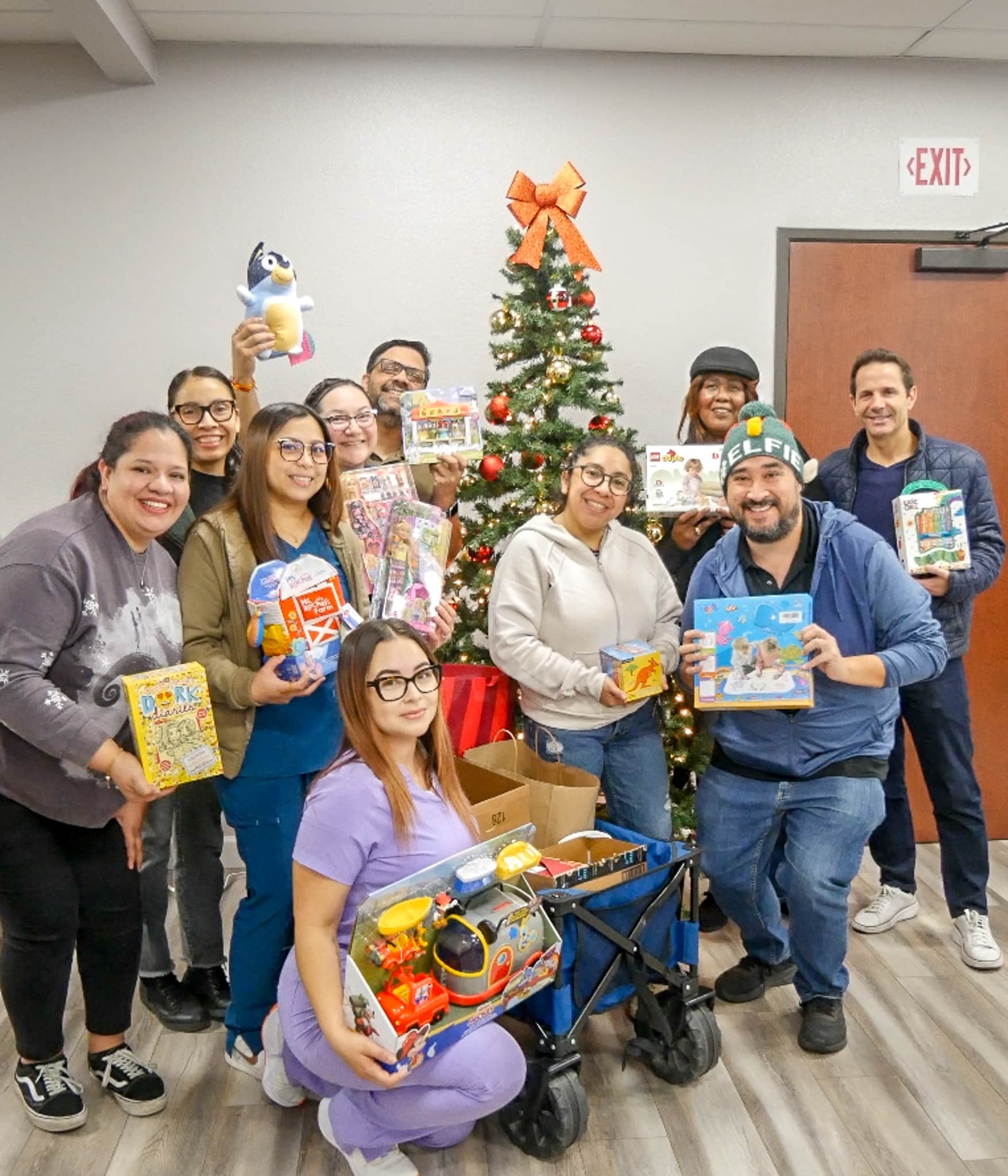 Group of healthcare professionals holding toys in front of a Christmas tree