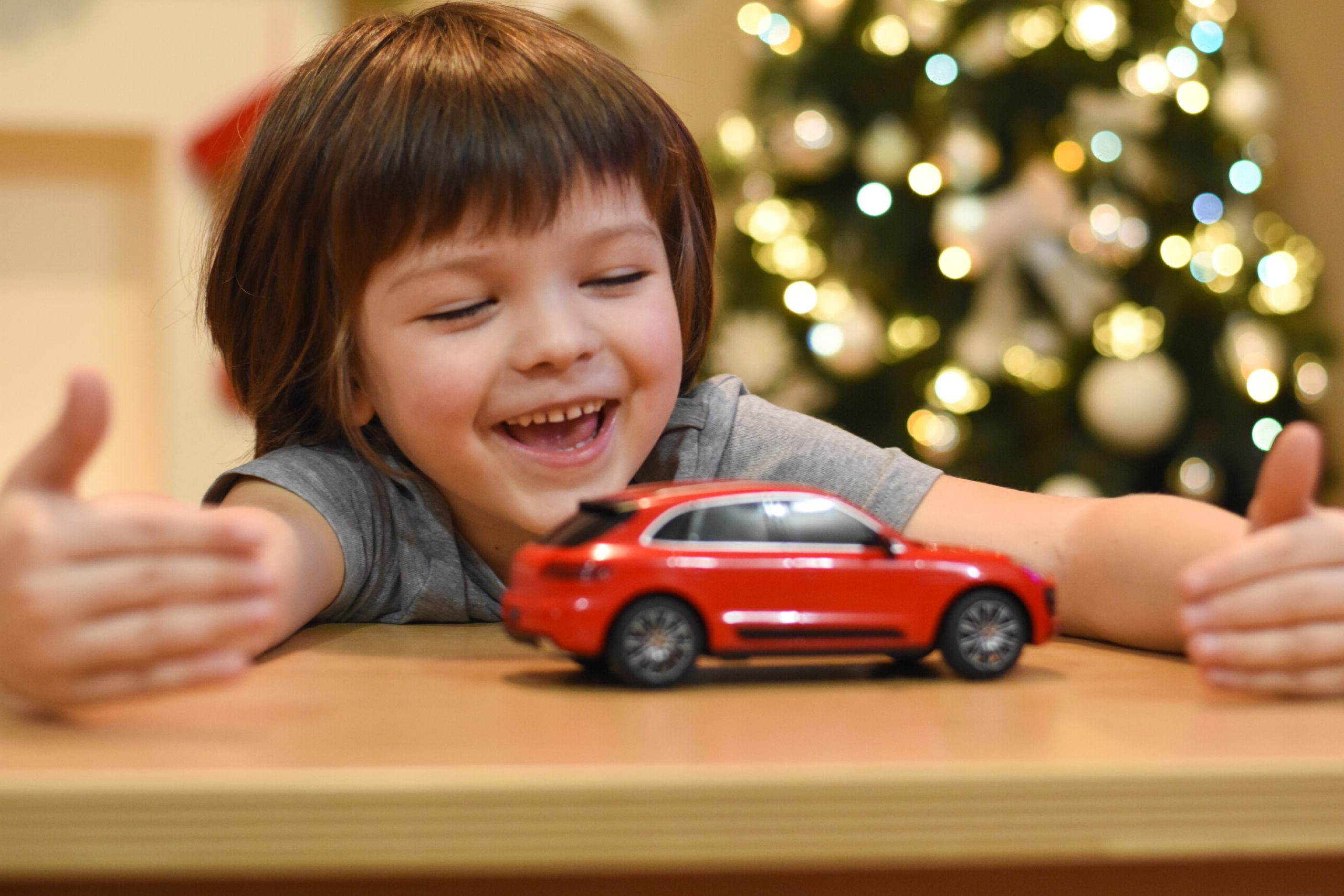 Niño sonriente jugando con su coche de juguete rojo con un árbol de Navidad de fondo